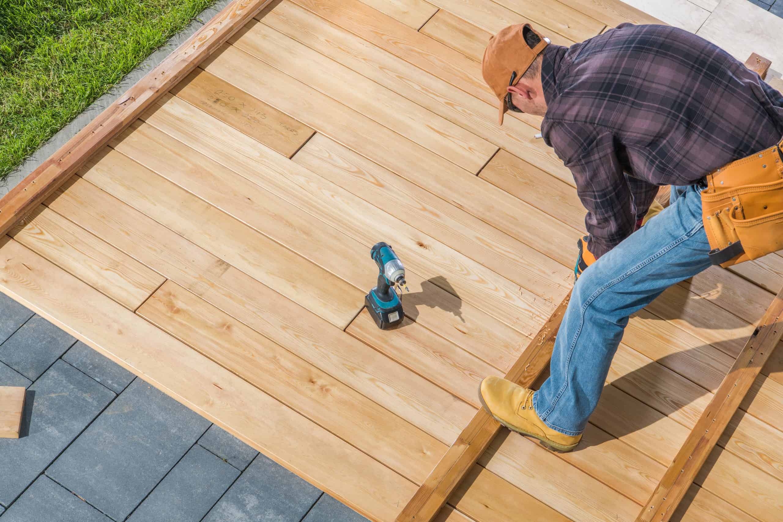 A man in a plaid shirt and orange cap is expertly constructing a wooden deck, embodying the craftsmanship of a general contractor in Orange County, NY.