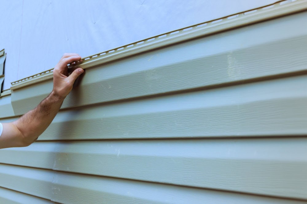A person’s hand is touching beige vinyl siding, demonstrating the quality of siding installation in Dutchess County, NY.