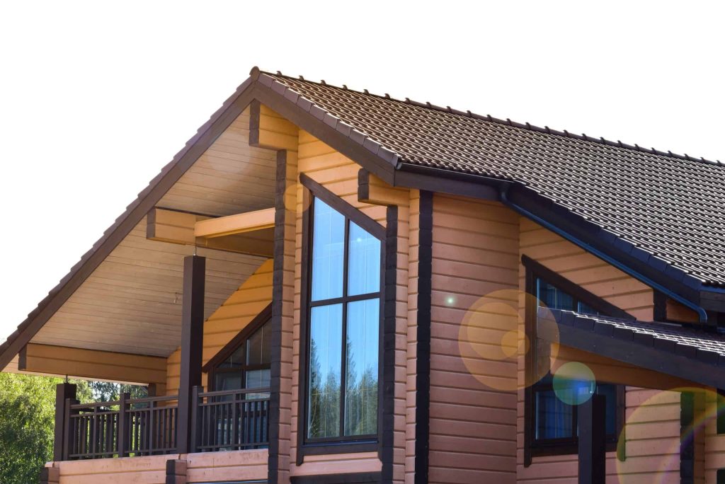 A modern log house with a dark shingled roof and large triangular windows gleams under the sun flares.