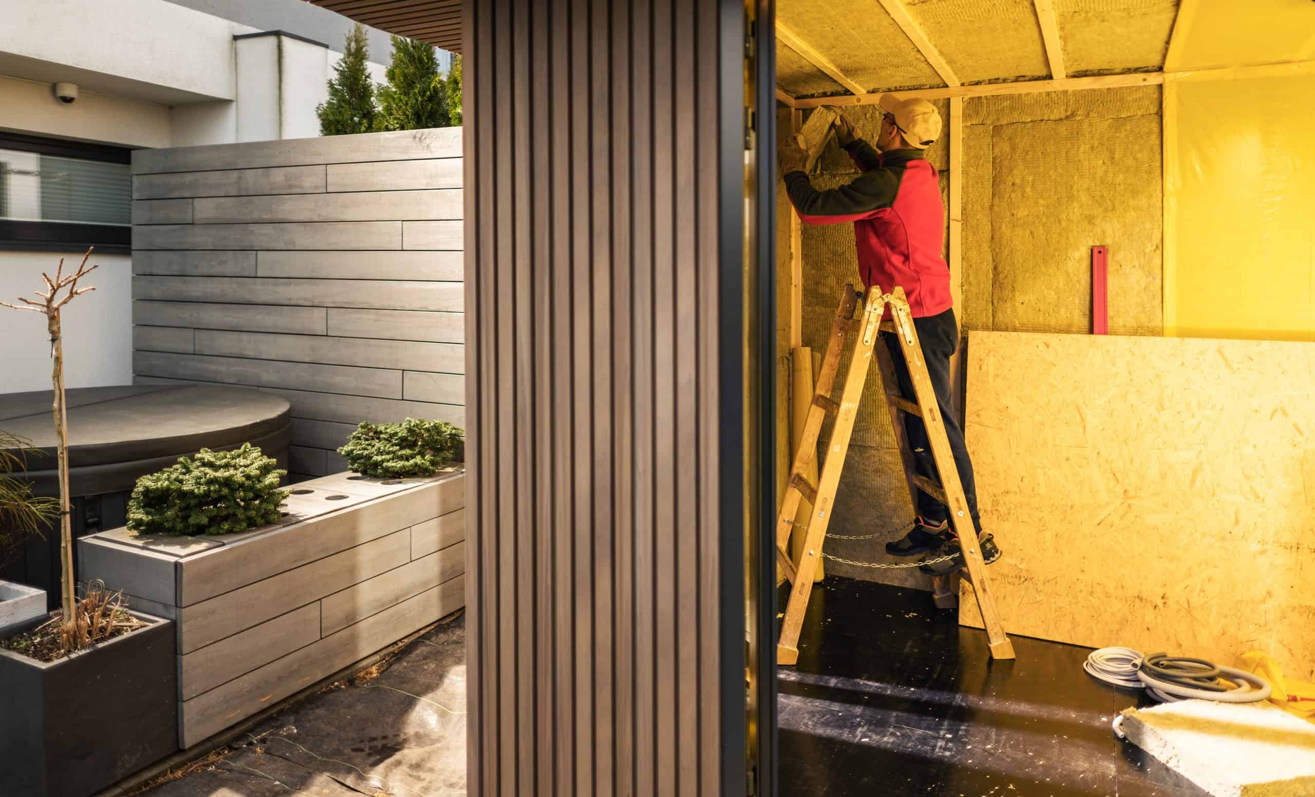 A person standing on a ladder is busy with insulation installation inside a partially constructed room.