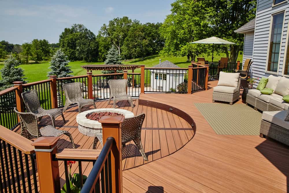 This wooden deck, ideal for home remodeling in Orange County, NY, boasts a circular design with wicker chairs encircling a stone fire pit.