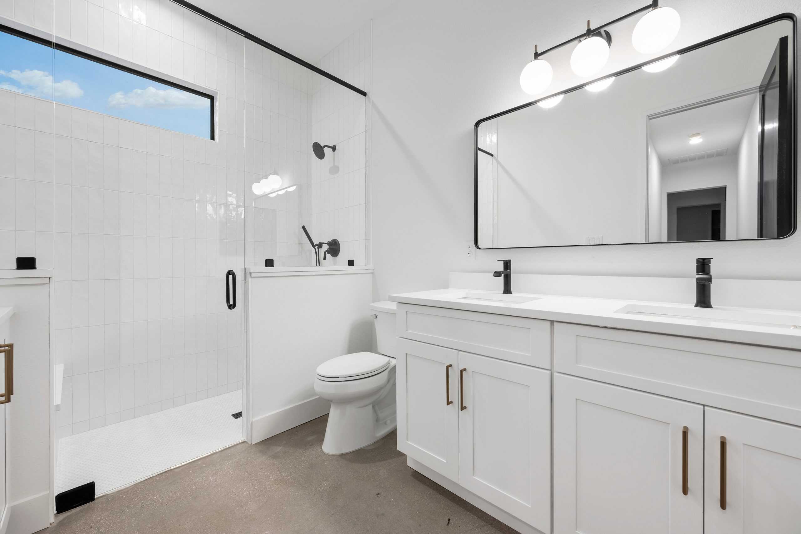 Modern bathroom with white walls and cabinets, a large rectangular mirror, and double sink.