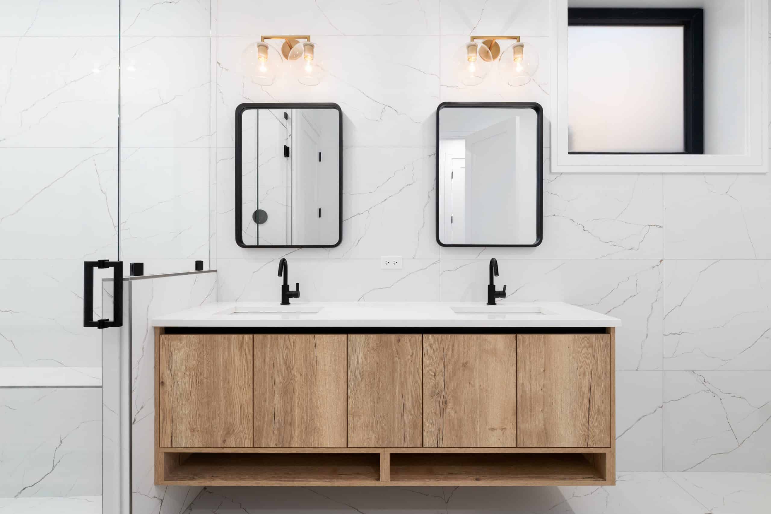 A modern bathroom in Orange County, NY features a double vanity with a wooden cabinet, two rectangular mirrors, and black faucets.