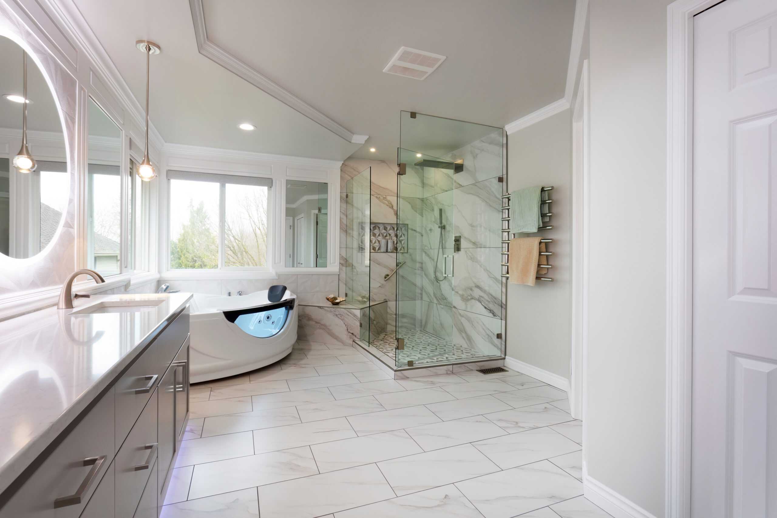 A modern bathroom with large windows, featuring a freestanding bathtub, a glass-enclosed shower with marble tiles, and sleek cabinetry.