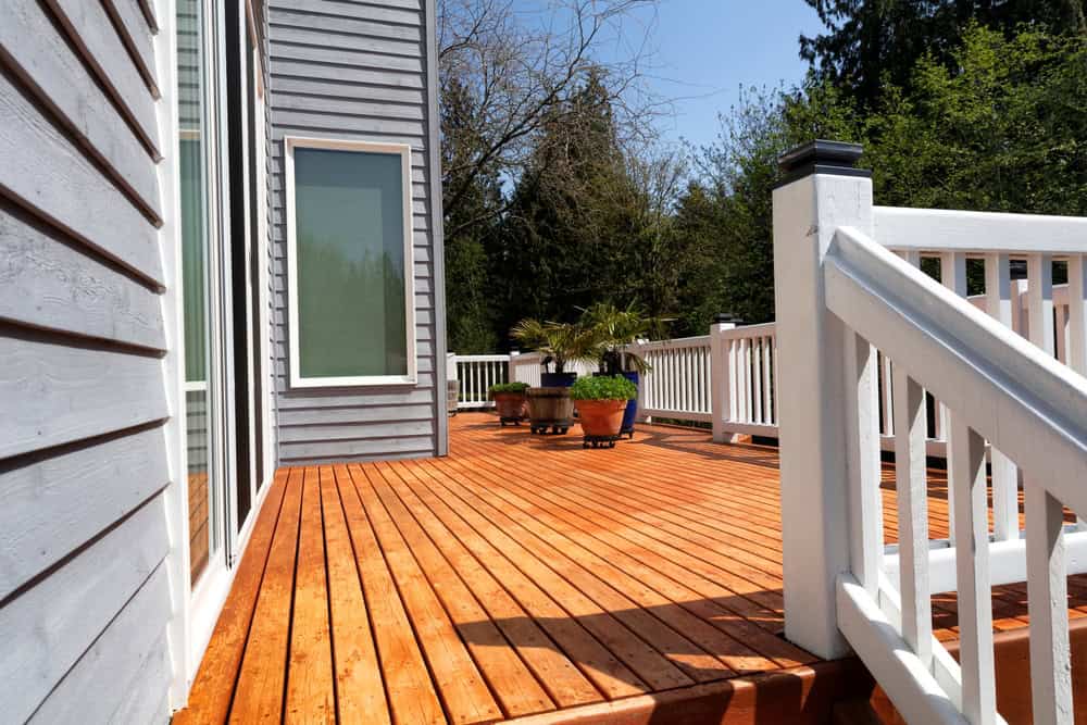 A sunlit wooden deck attached to a gray house, perfect for home remodeling in Orange County, NY.