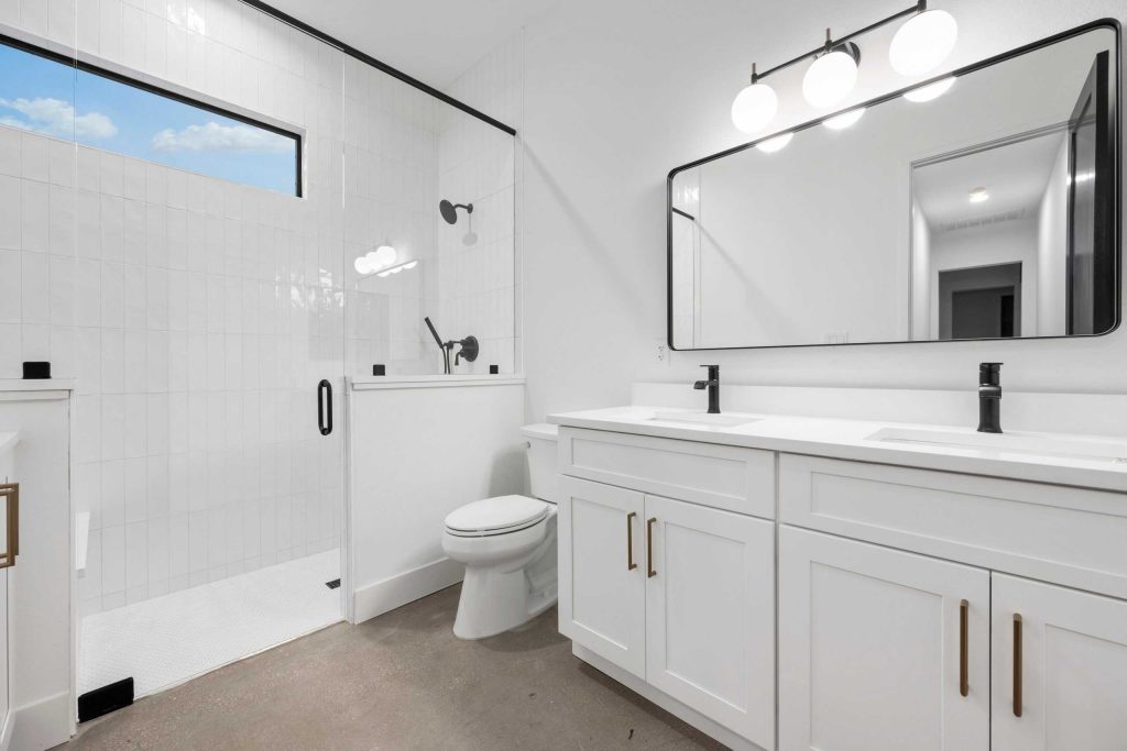 A modern bathroom with a large mirror and double vanity featuring black faucets and white cabinets.