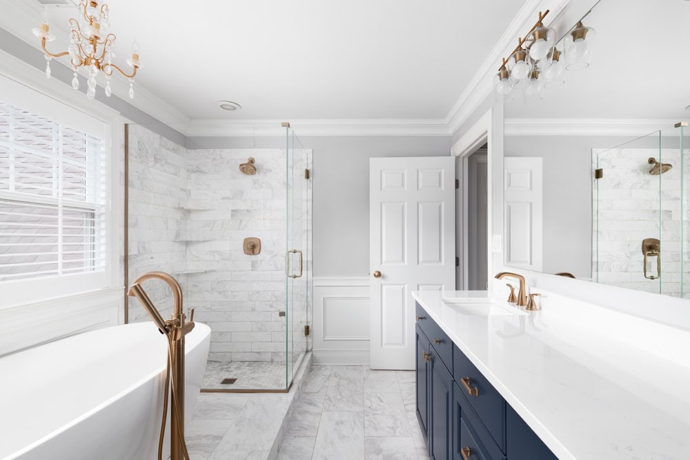 Elegant bathroom with white marble floors and walls, featuring a freestanding bathtub and glass-enclosed shower.