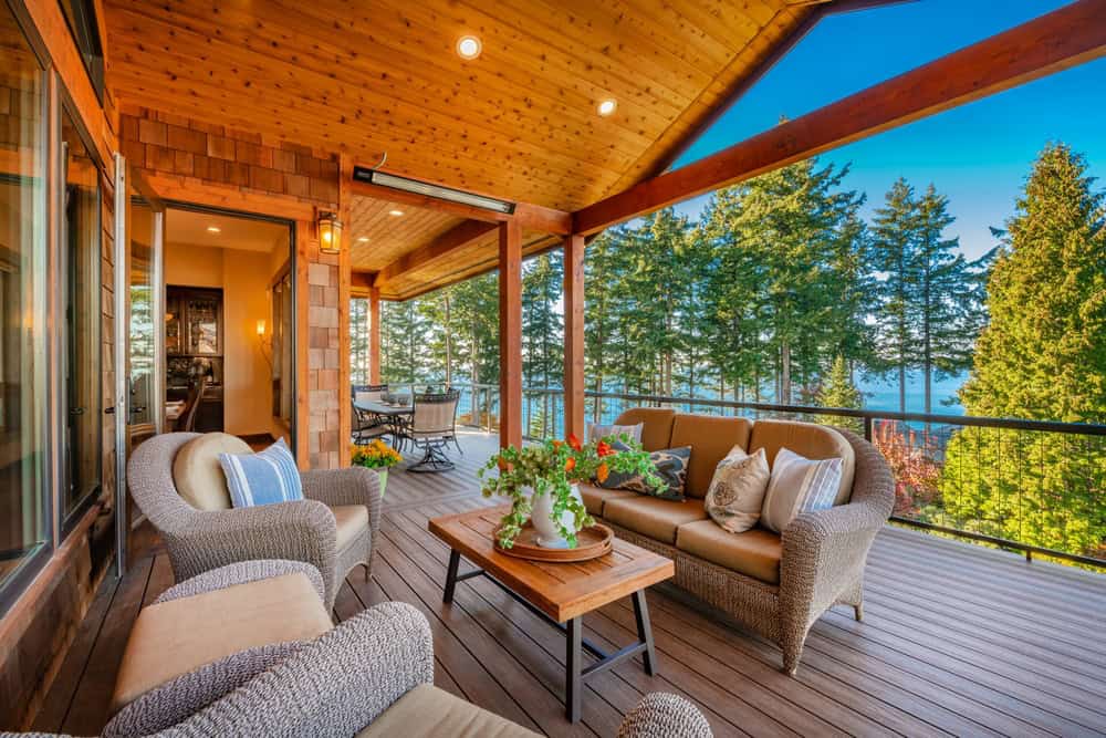 A cozy outdoor patio with wicker furniture and cushions under a wooden roof invites relaxation.