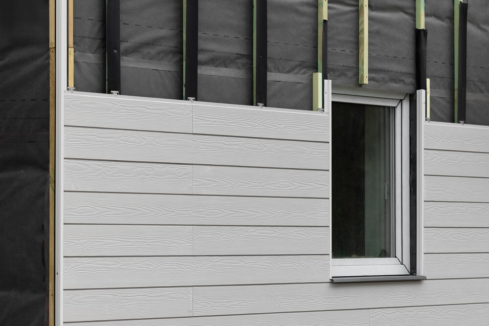 Close-up of a building facade under construction with partially installed horizontal white siding panels, executed by a general contractor.