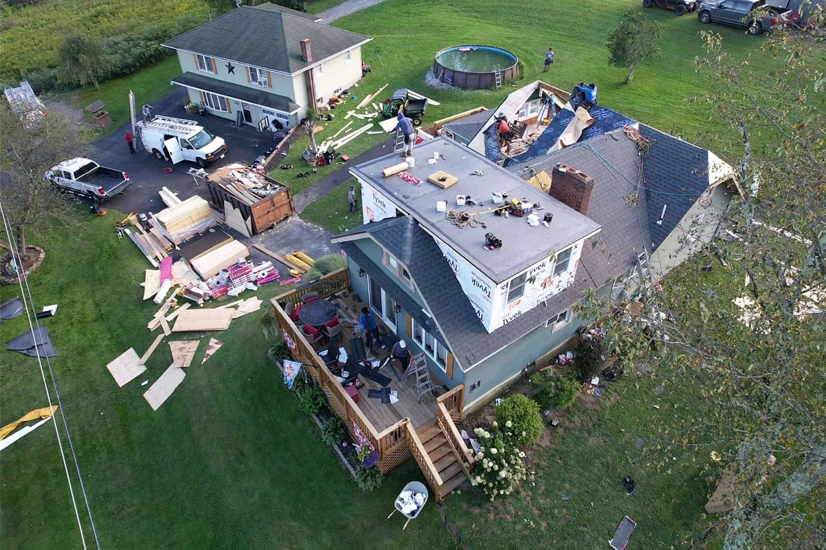 Aerial view of a house under renovation. Roofing materials and tools are scattered around the yard.