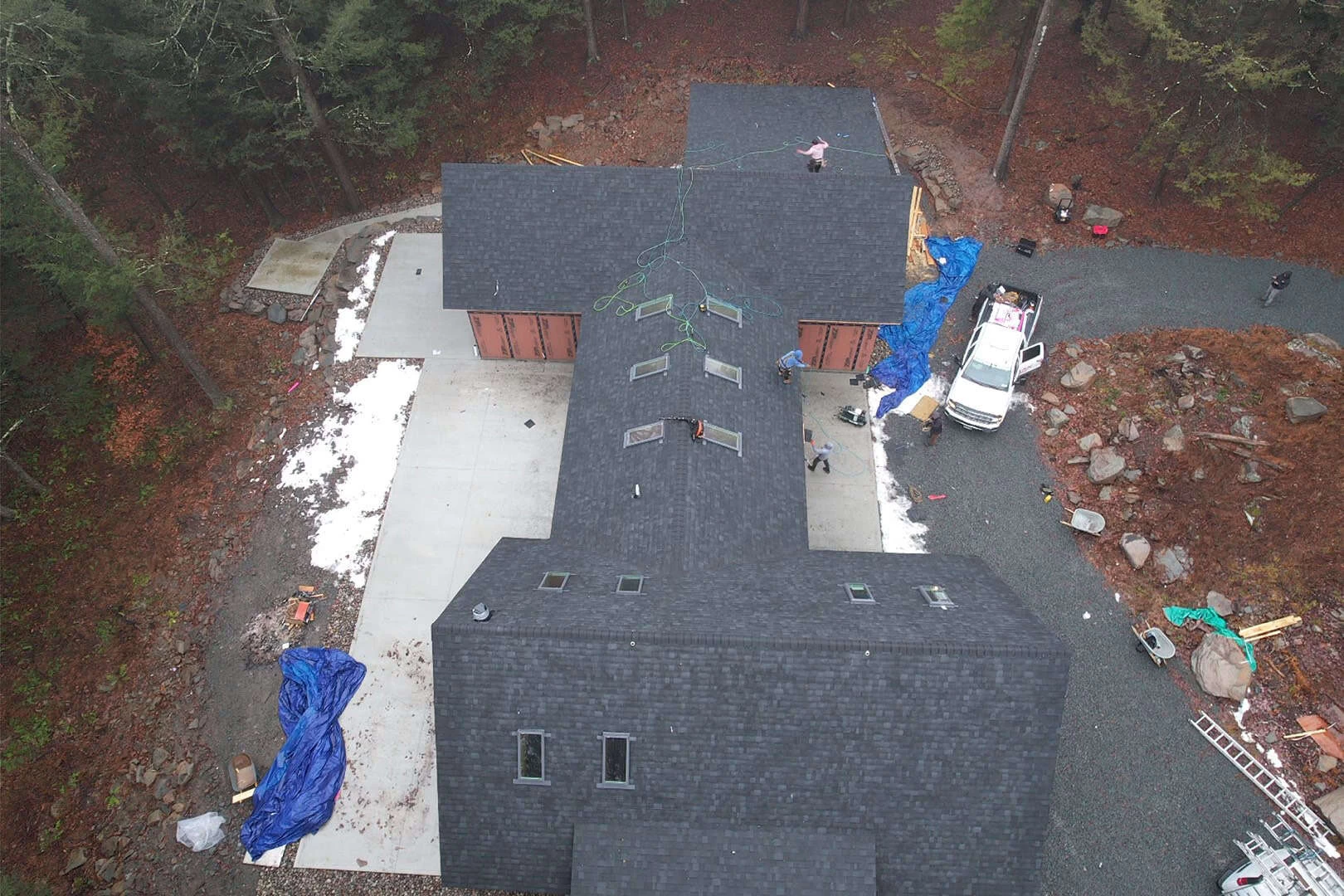 Aerial view of a black-roofed house under construction, surrounded by trees.