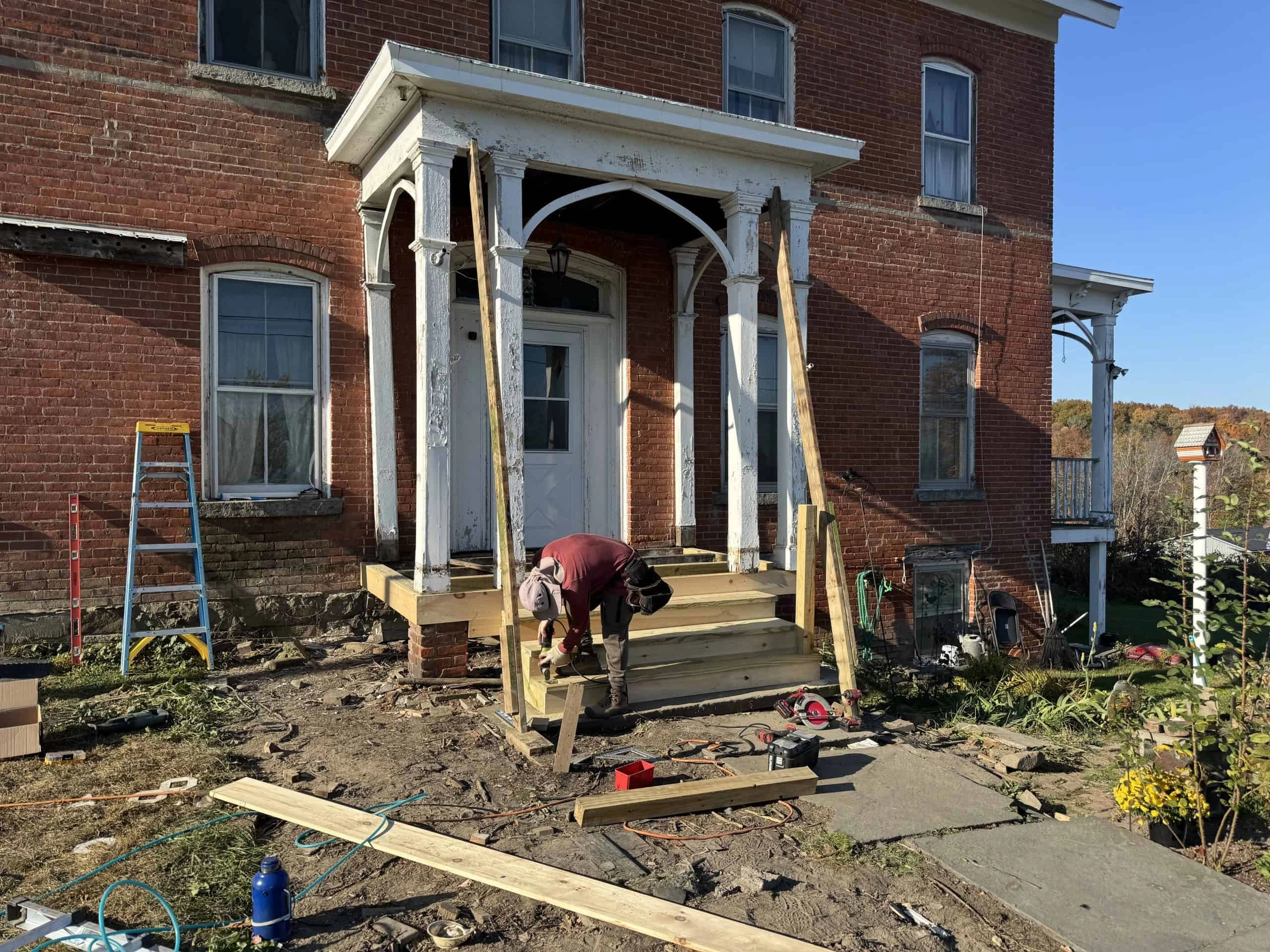 A person is working on the wooden steps of a brick house with a porch.