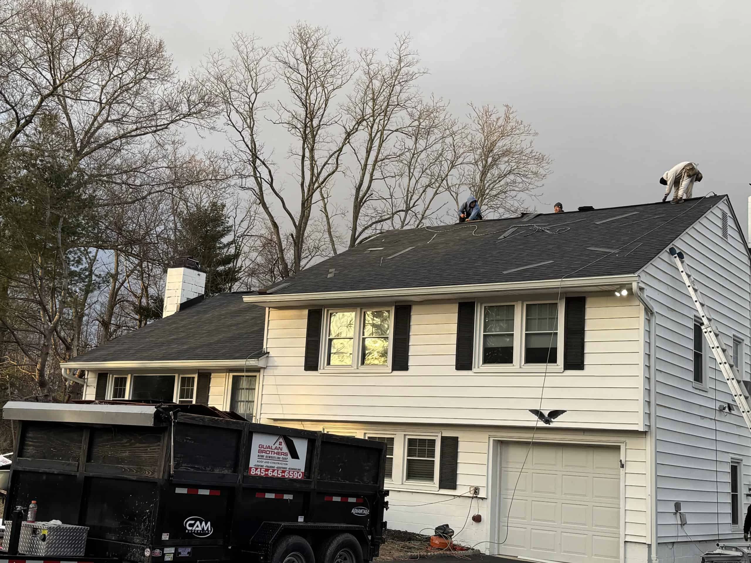Workers are installing a new roof on a two-story white house.