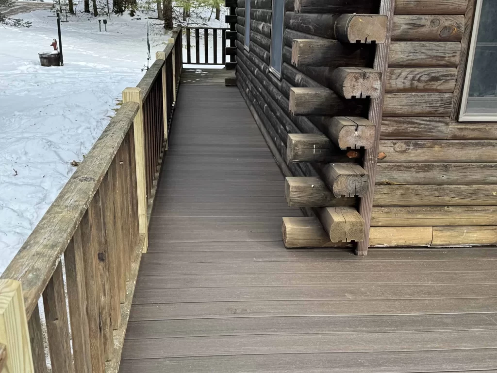 Wooden deck of a log cabin with snow on the ground surrounding it.