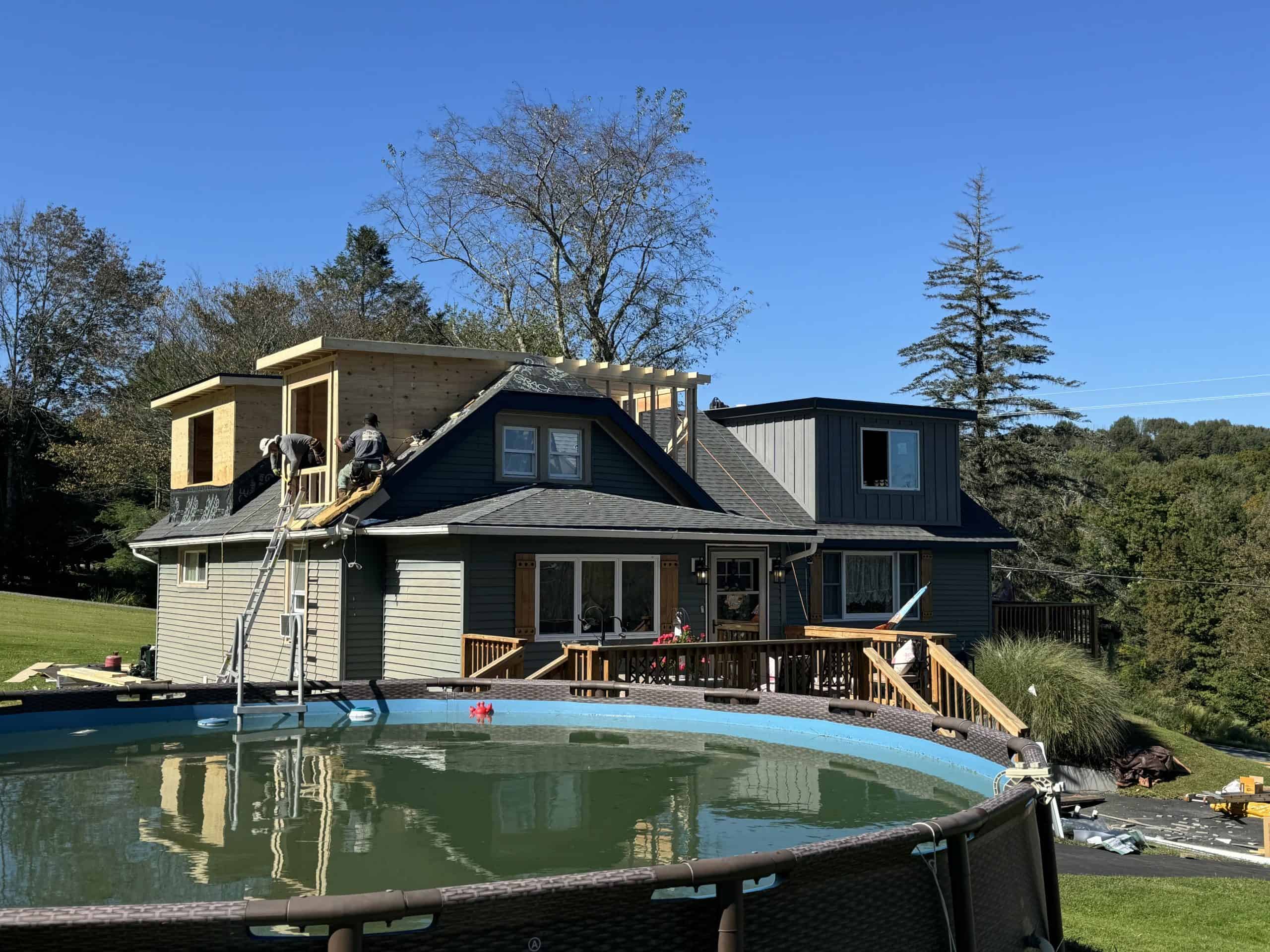 A house with a rooftop addition under construction, surrounded by trees.