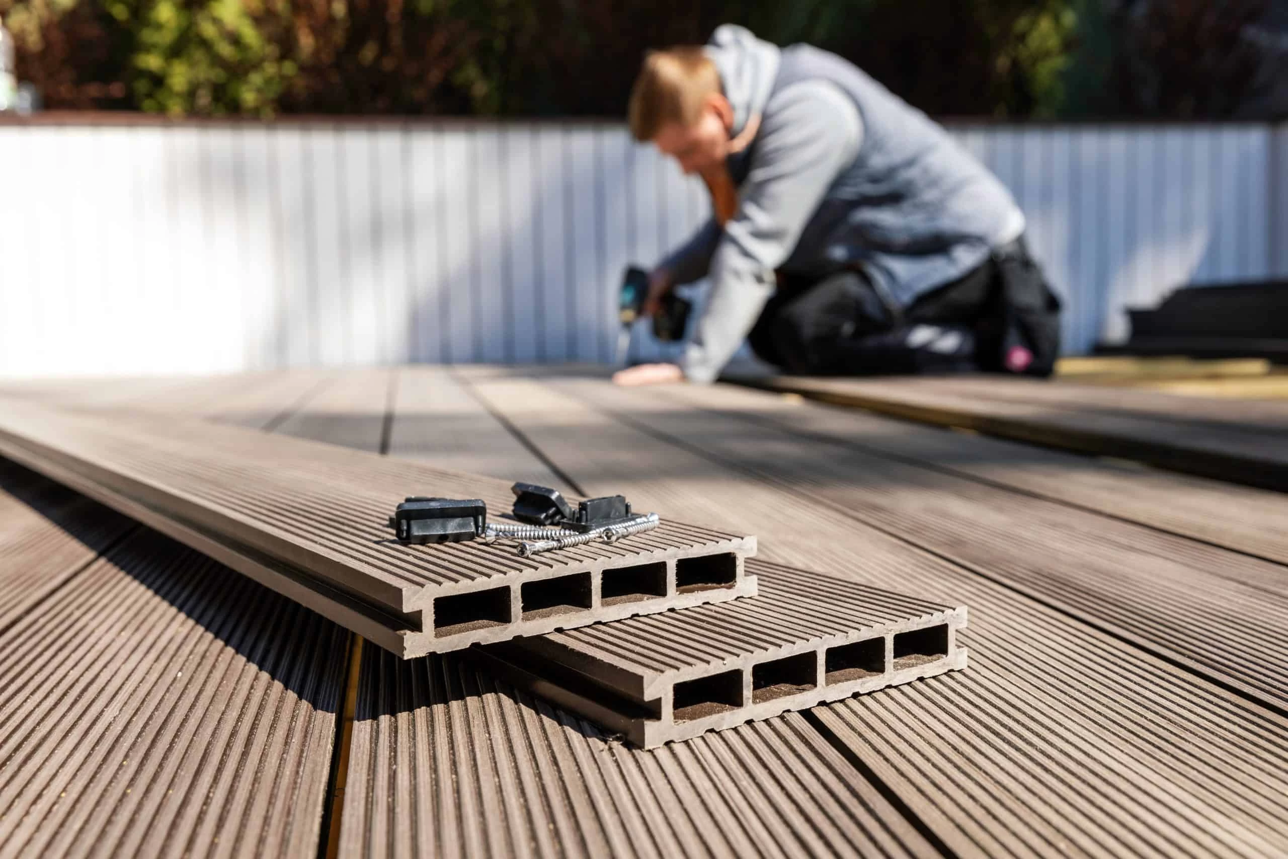 Close-up of composite decking boards stacked on a deck, with screws and fasteners on top.